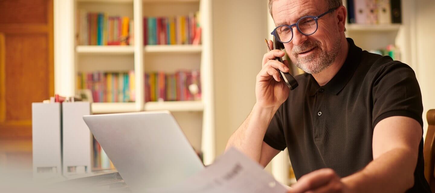 Small business owner talking on the phone while reviewing documents at a desk with a laptop, highlighting the importance of managing insurance coverage.