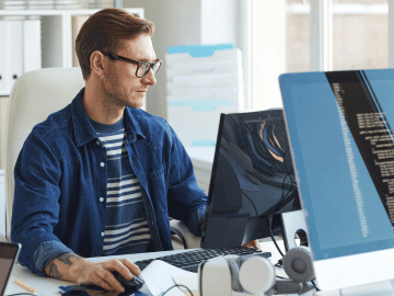 A male developer sits at a desk coding on a desktop computer