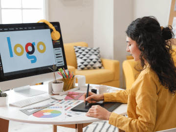 Female graphic designer sits at a computer using a drawing pad to design a logo