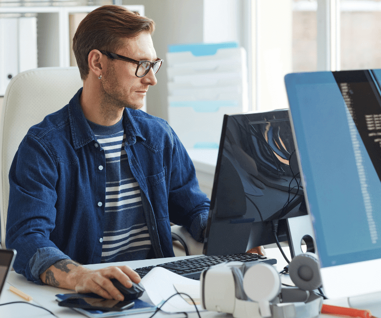 A male developer sits at a desk coding on a desktop computer