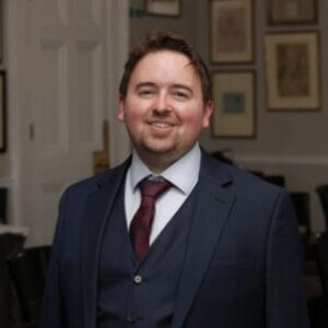 Dr Iain Campbell, Lead Director and Head of AI Policy, Ethics & Transformation at HLA Scotland, commentator on IR35 status. Blue suit & red tie, smiling