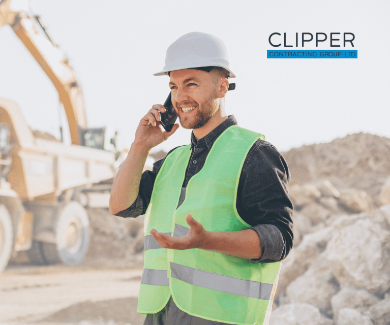 Construction worker on the phone standing on a construction site wearing a hard hat and high visibility vest