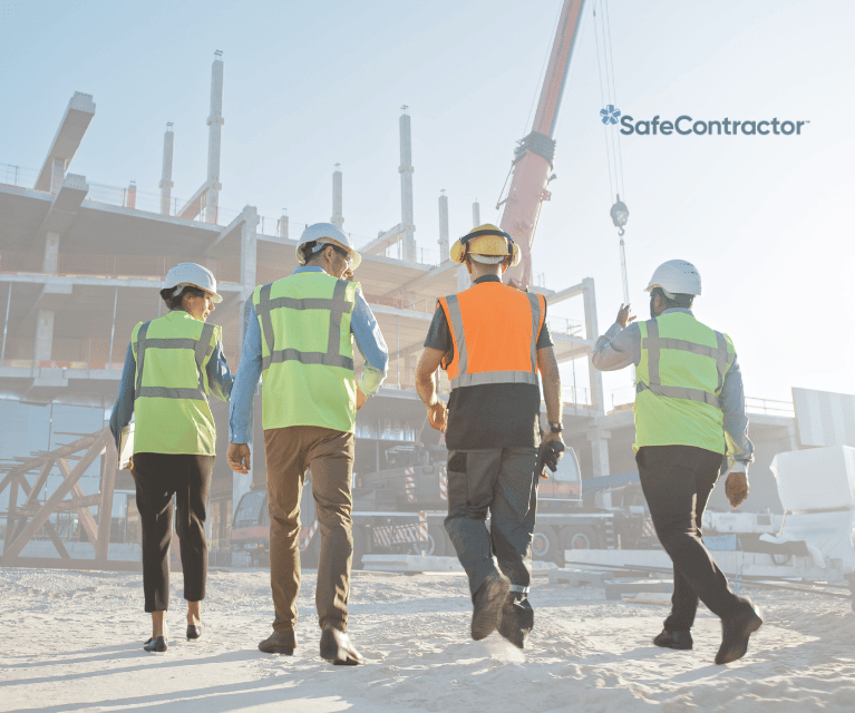 Group of workers walking through a construction site wearing high visibility vests, helmets and ear defenders.
